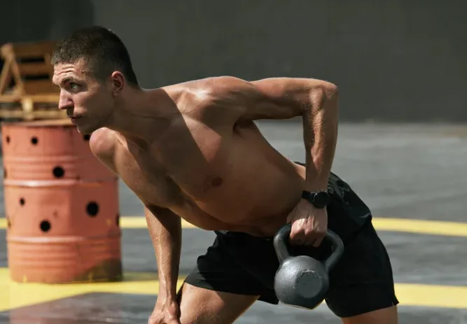 Shirtless man doing a bent-over single-arm kettlebell row