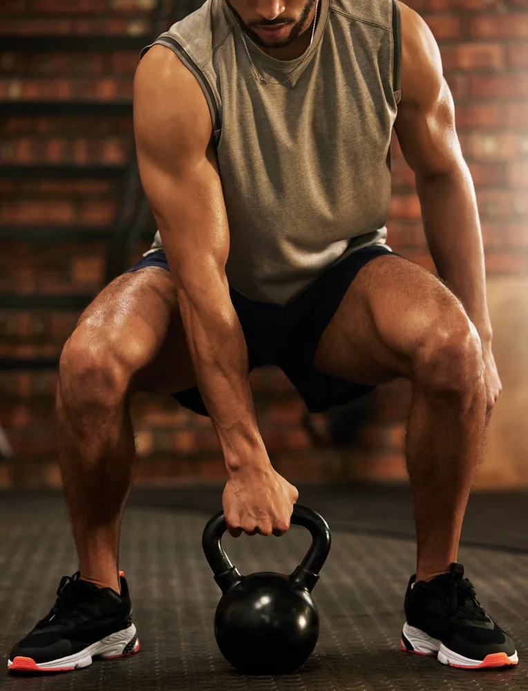 Man in a sleeveless top setting up over a kettlebell between his feet to start a clean