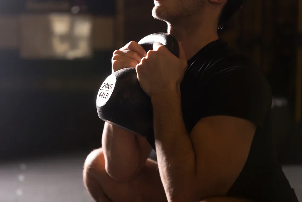 Close-up of a man holding a kettlebell by the horns at his chest for a goblet squat