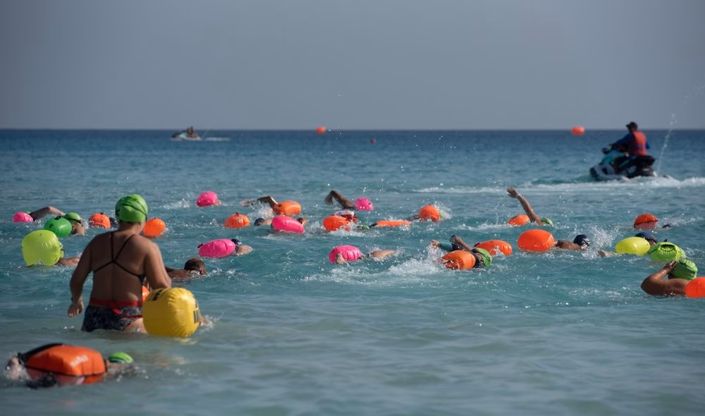 A pack of ocean swimmers wearing colourful safety buoys navigate toward the first turn