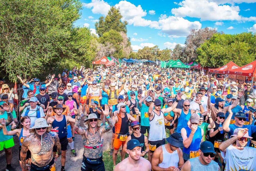 A large crowd of runners with hands raised at the start of an Australian backyard ultra