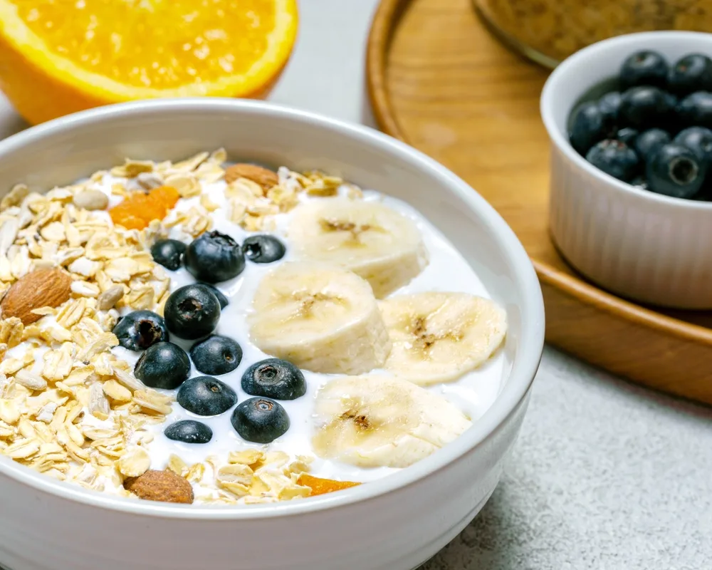 A bowl of Greek yoghurt topped with oats, banana slices, blueberries and almonds, a high-protein breakfast bowl option