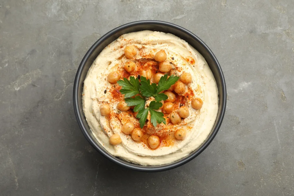 A bowl of hummus topped with whole chickpeas, paprika and parsley, a plant-based protein option for a vegetarian breakfast