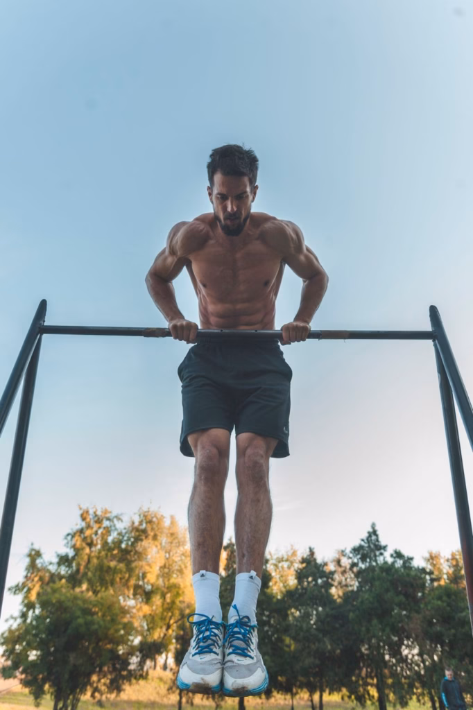Man holding an L-sit style dip at the top of an outdoor pull-up bar, core and shoulders braced.