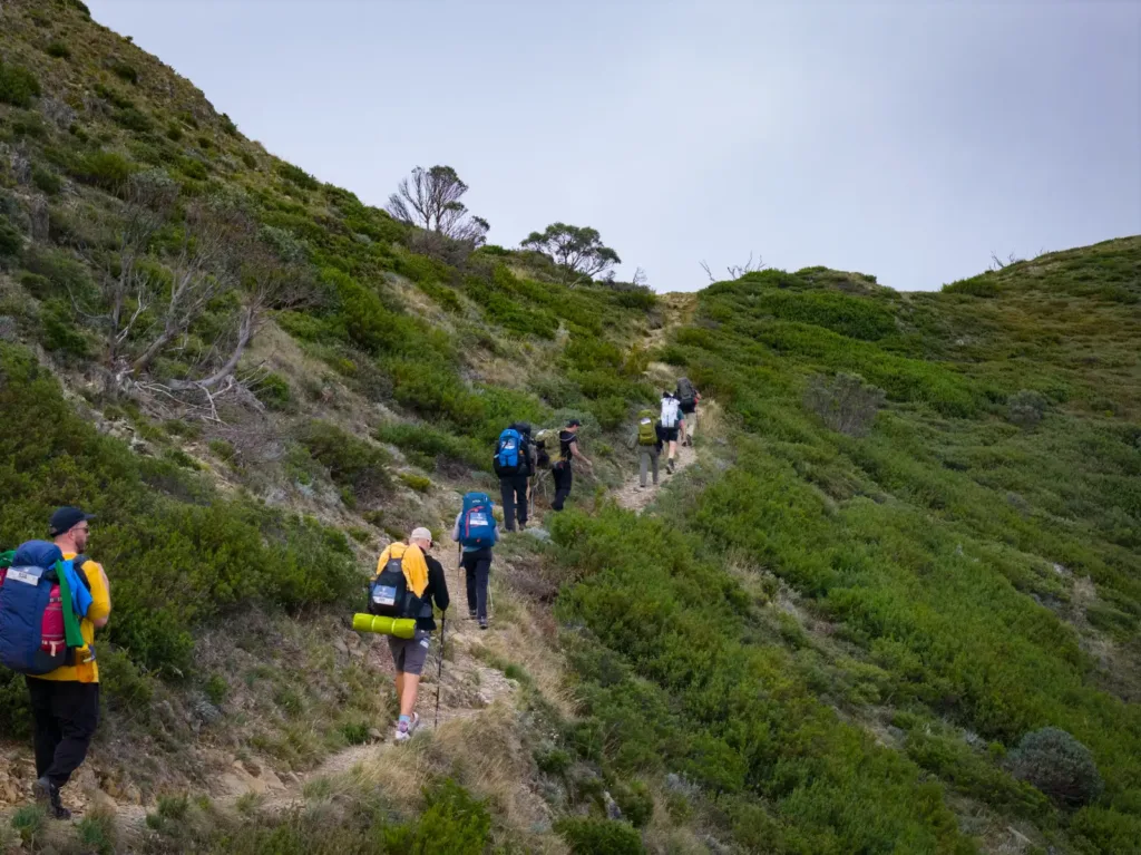 Hikers with backpacks walking along an open hillside trail on a HIGHLANDER Adventure hike