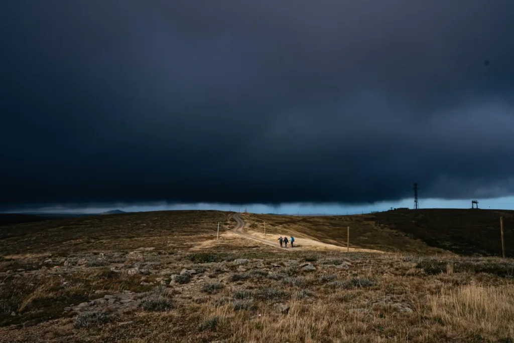 Hikers walking along an alpine ridge track as dark storm clouds roll in overhead