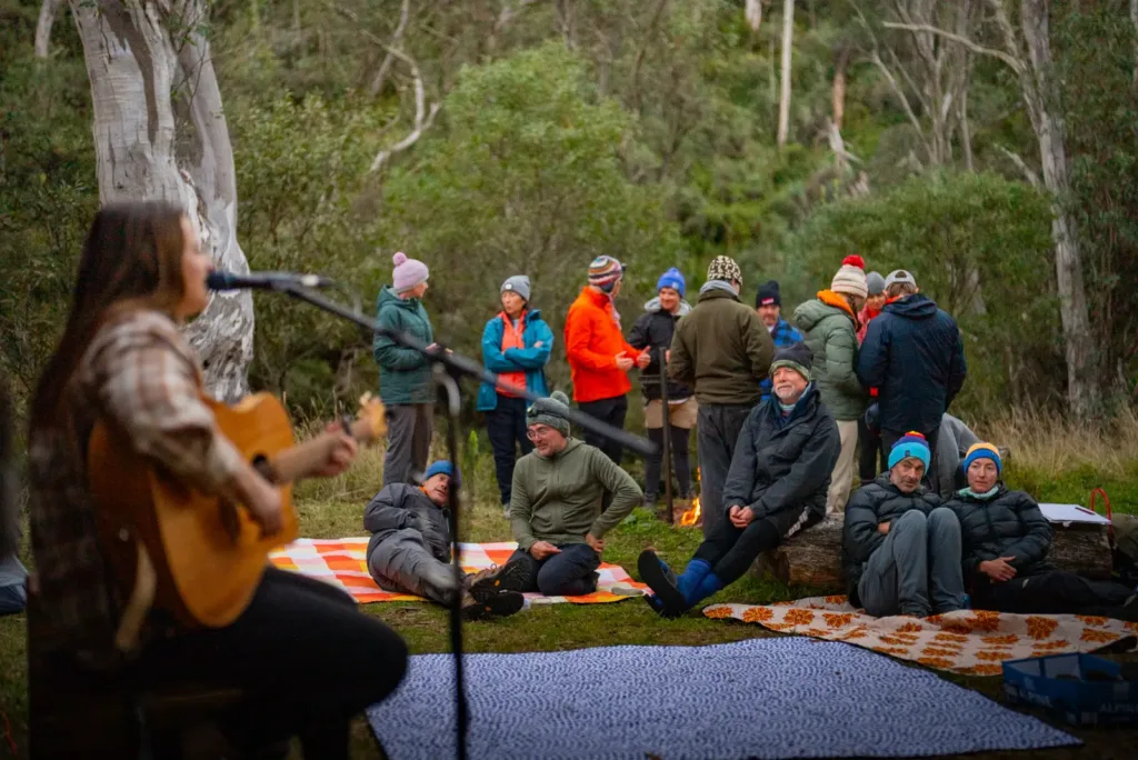 A woman playing guitar and singing for a group of hikers gathered around a campfire