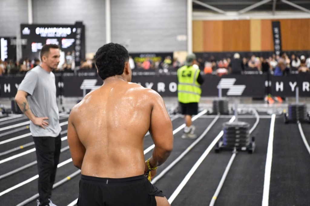 A sweaty HYROX competitor standing near the sled track at a HYROX event