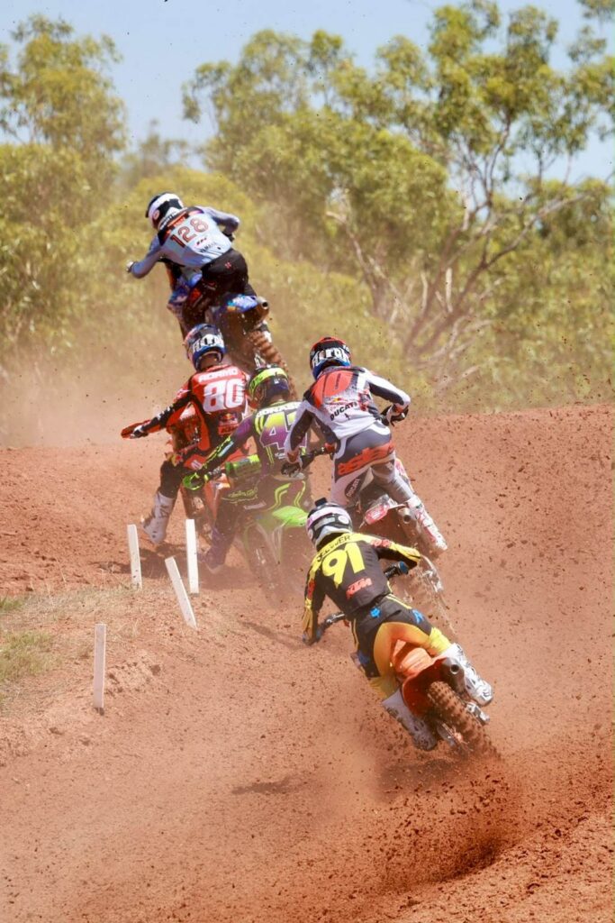 A group of motocross riders airborne together over a jump during MXGP racing at Hidden Valley, Darwin