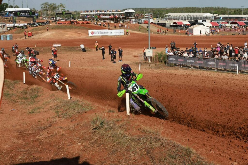 Wide view of the Hidden Valley Motorsport Complex track with fans lining the fence as a rider corners through a bermed turn