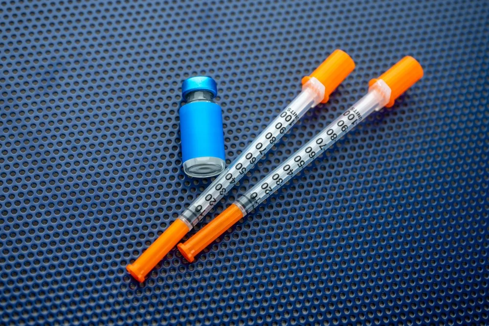 Two insulin syringes beside an unlabelled vial, the kind of equipment used for at-home peptide injections
