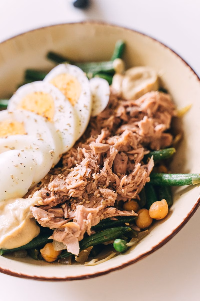 Bowl of flaked tuna with sliced boiled egg, green beans, chickpeas and hummus