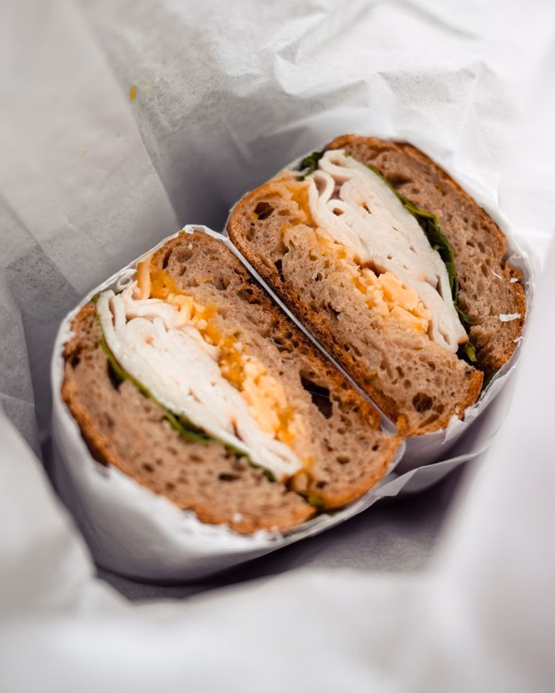 Halved turkey and cheese sandwich with salad leaves on wholegrain bread, wrapped in paper