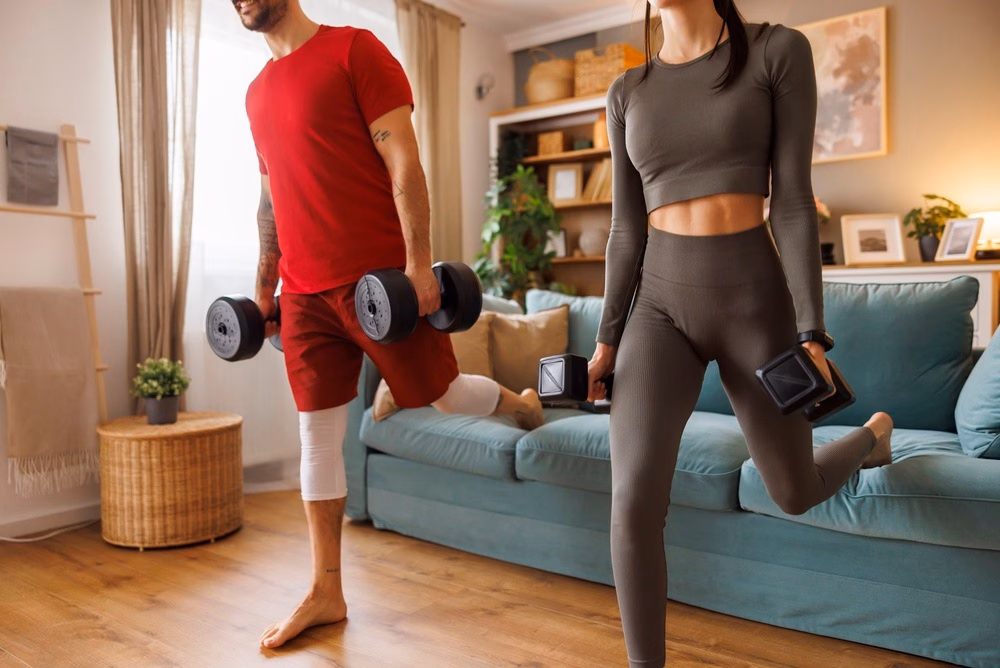 A man and woman performing dumbbell Bulgarian split squats at home using a couch for rear-foot elevation