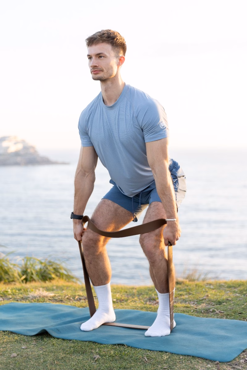 A man performing a standing banded exercise with the band looped under his feet, held at hip height