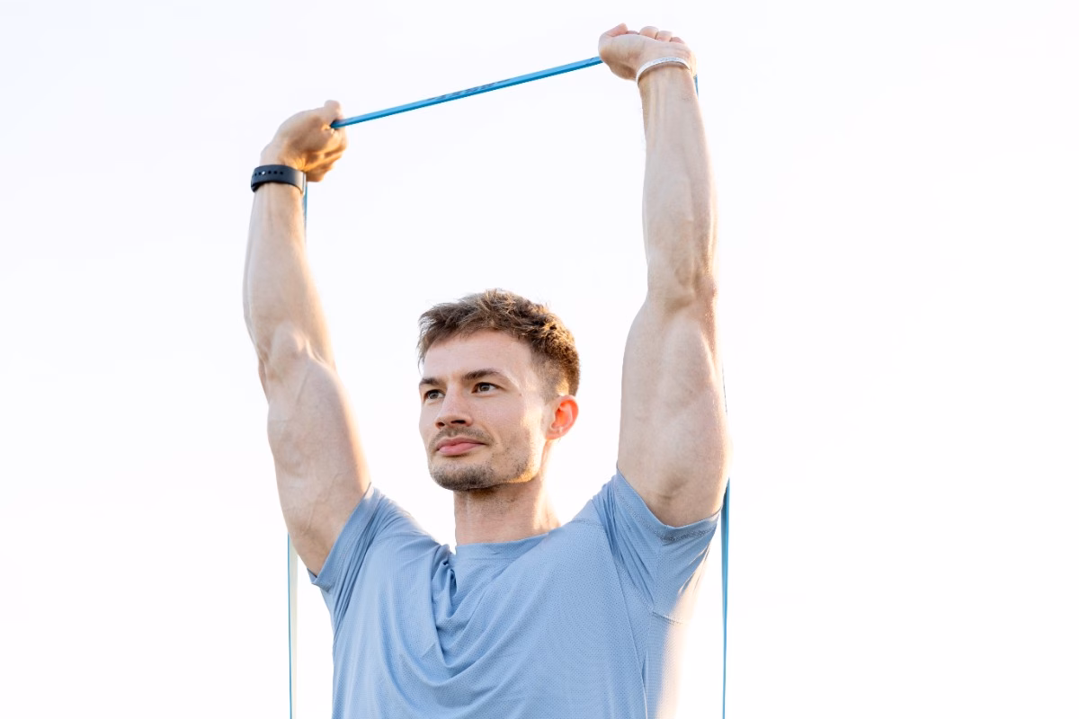 A man stretching a resistance band overhead with both arms extended, a shoulder mobility warm-up