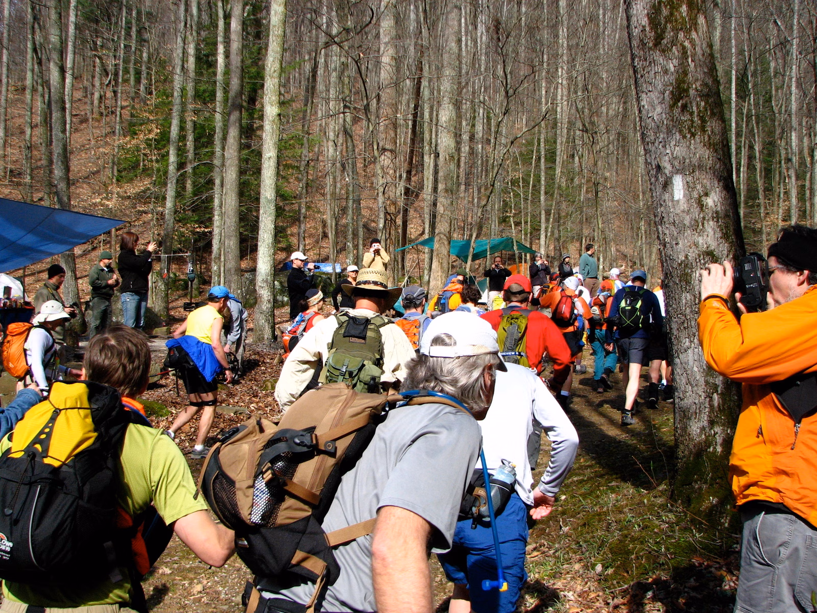 Runners with backpacks heading up a wooded trail at the start of the 2009 Barkley Marathons, watched by spectators with cameras