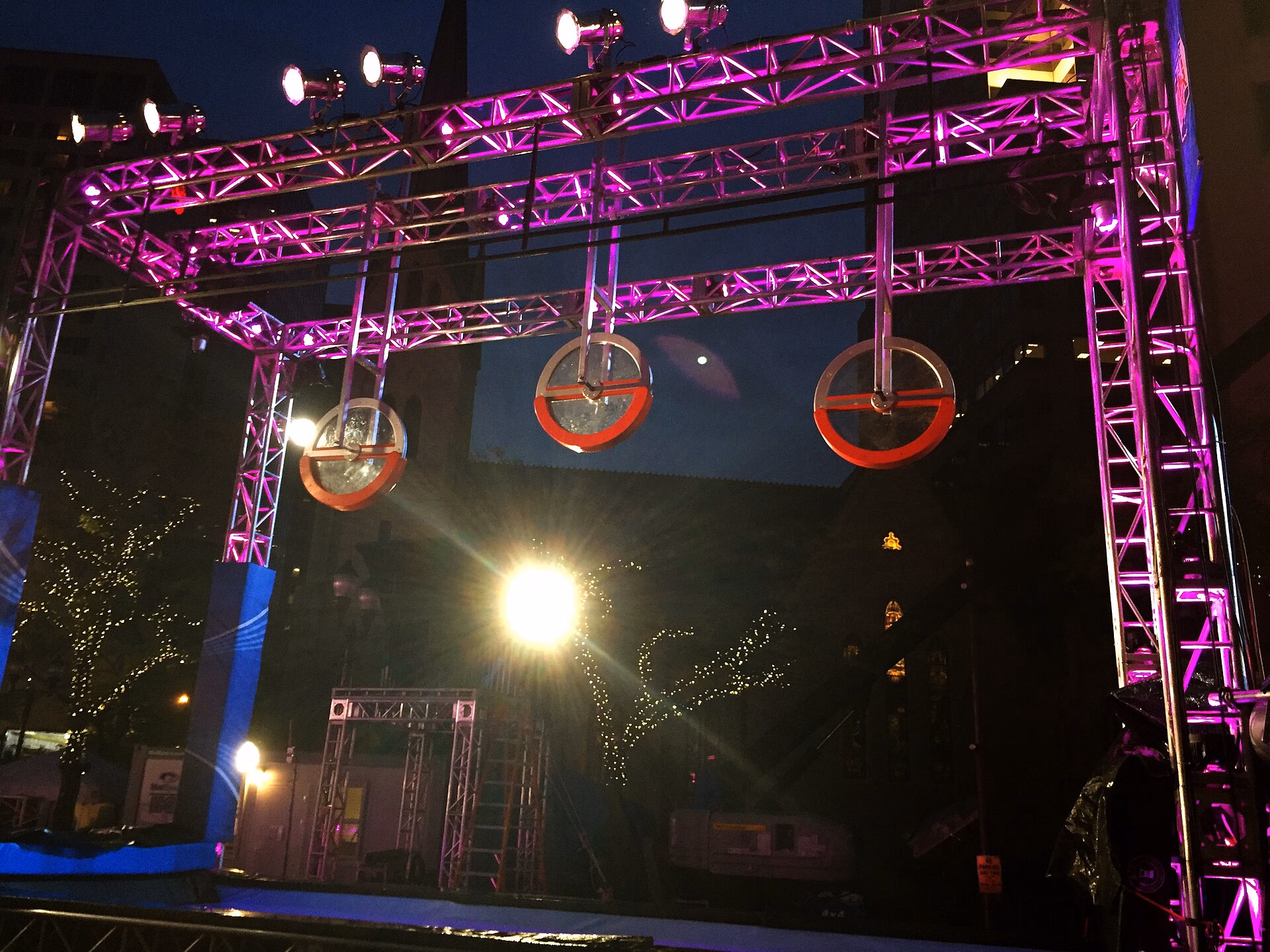 Three red-rimmed wheels hanging from a lit frame on an American Ninja Warrior course