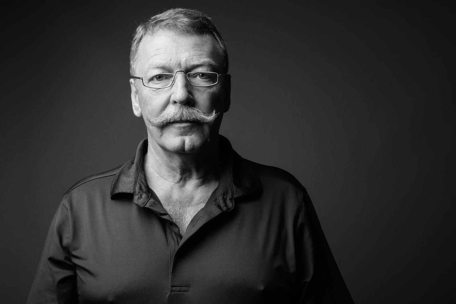 Older man with glasses and a grey handlebar moustache waxed up at the tips