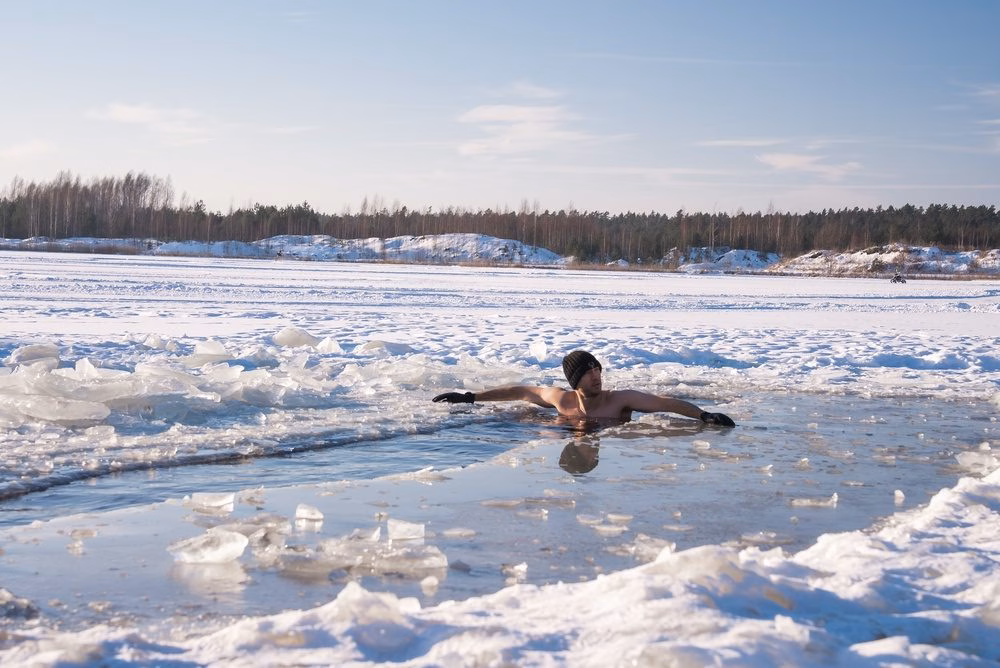 A man wearing only a beanie and gloves swims in a hole cut in the ice of a frozen lake