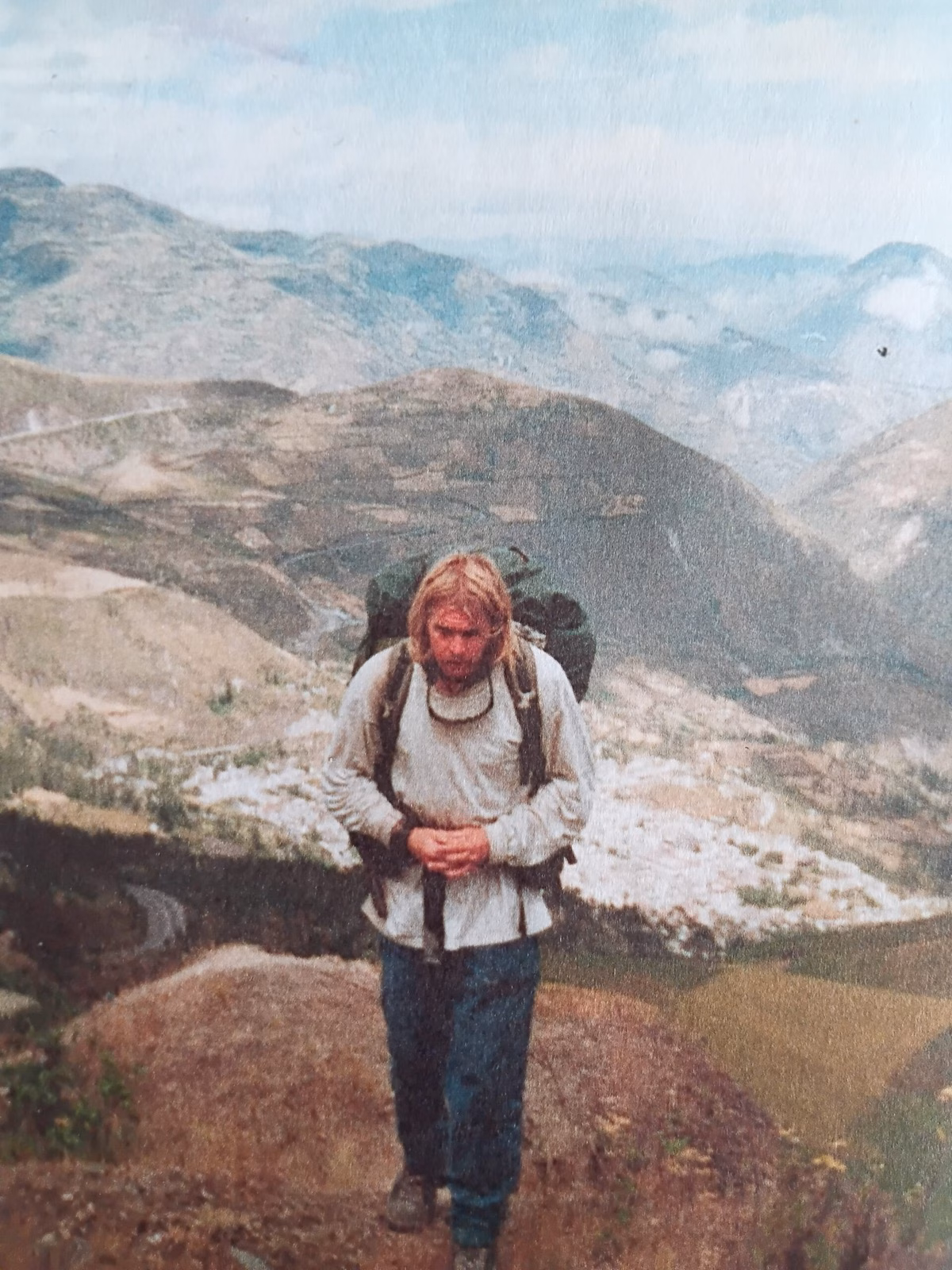 Karl Bushby with a large backpack on a mountain path, valleys behind him