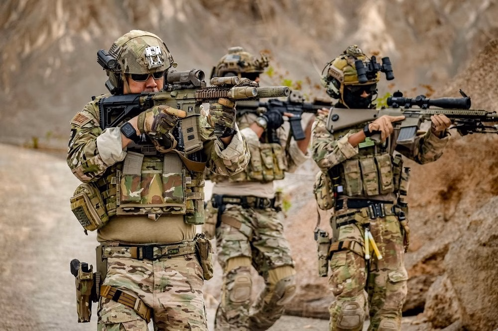 Three soldiers in camouflage and combat gear aiming rifles during tactical training