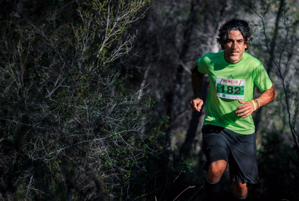 Trail runner in a green race shirt running through dark bush